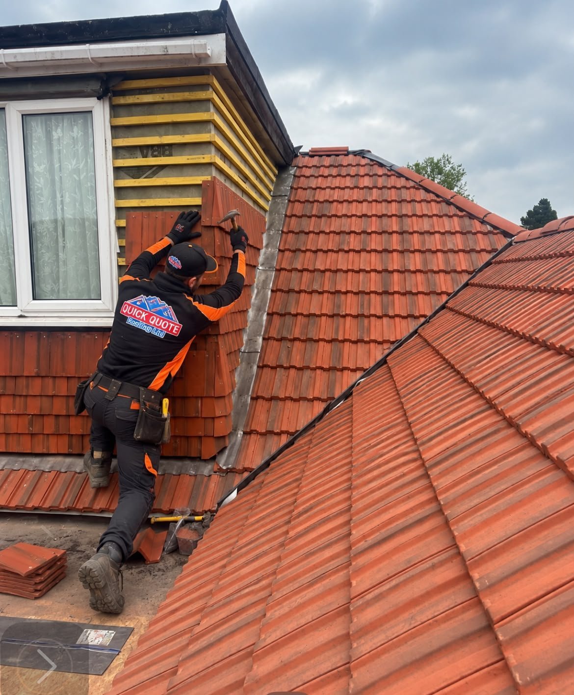 Roofer in safety harness working on clay tile roof next to dormer window